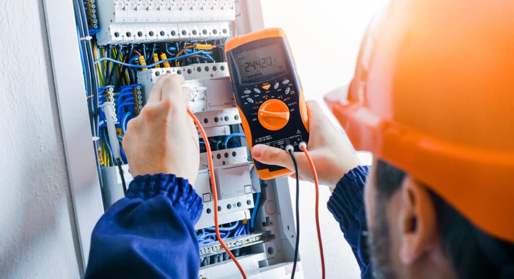 Électricien mesurant la tension (244.20 V) sur un tableau électrique résidentiel avec disjoncteurs "B 16" et câbles. Sécurité.