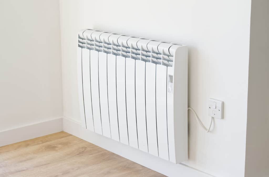 Radiateur électrique mural blanc avec thermostat intégré, sur mur clair et parquet. Ambiance moderne.